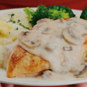 Close up of person holding a play of broccoli, mashed potatoes and chicken with mushroom soup on top